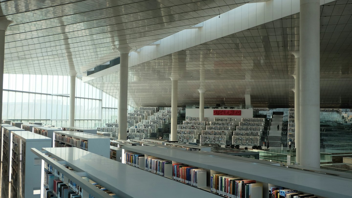 People walk between white bookshelves in a modern library.